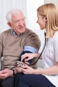 Nurse taking elderly patient's blood pressure in their home.
