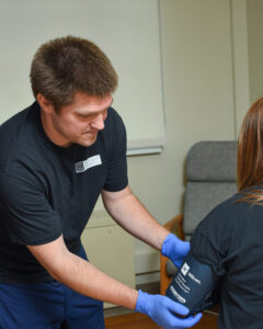 Matthew Clark, CNA, securing a blood pressure cuff on a patient's arm.